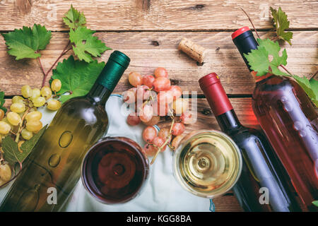 Vino rosso e bianco di bicchieri e bottiglie su sfondo di legno. uve fresche e i mosti di uve lascia come decorazione, vista dall'alto Foto Stock