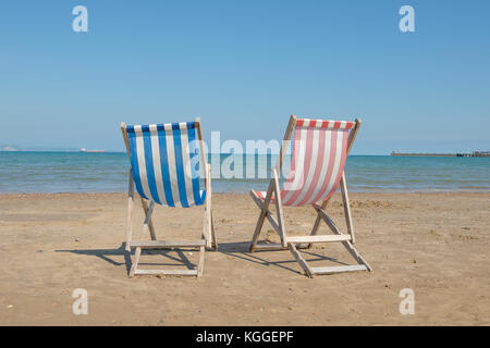 Due biancheria da vuoto sedie da spiaggia una blu e una rossa al centro dell'immagine sulla spiaggia di weymouth del Regno Unito, di fronte al mare su un soleggiato Foto Stock