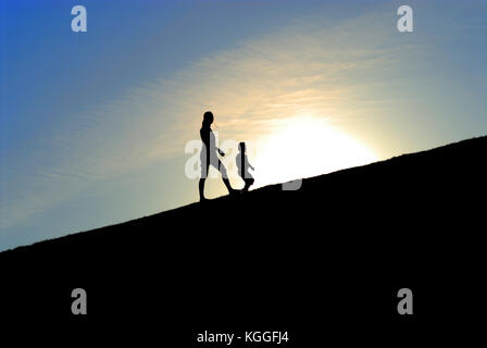 Silhouette di due ragazze a piedi su per la collina insieme contro il sole Foto Stock