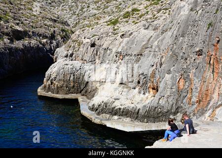 Tre giovani seduti sui passi che si affaccia sulla baia al punto di partenza, Blue Grotto, Malta, l'Europa. Foto Stock