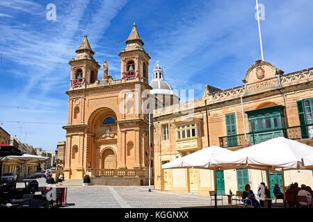 Le persone in un momento di relax a caffetterie con la chiesa parrocchiale di Nostra Signora di Pompei alla parte posteriore, Marsaxlokk, Malta, l'Europa. Foto Stock