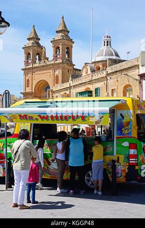 I turisti in coda per gelato in un gelato van con la chiesa parrocchiale di Nostra Signora di Pompei alla parte posteriore, Marsaxlokk, Malta, l'Europa. Foto Stock