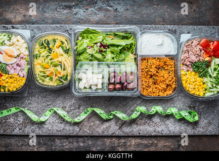 Varie pranzo sano caselle nella confezione di plastica verde e nastro di misurazione su sfondo rustico, vista dall'alto. dieta concetto alimentare. Foto Stock