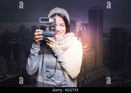 Cattura momenti felici bella giovane donna in un Caldo berretto lavorato a maglia a sorridere mentre si scatta una fotografia con un aiuto di una foto istantanea telecamera Foto Stock