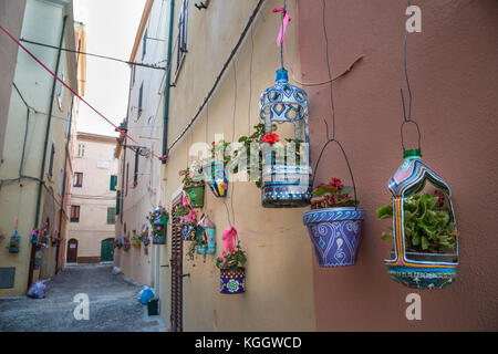 Fiori in decorate a mano appesa fioriere fodera una stretta di ciottoli pietra vicolo di Alghero, Sardegna Foto Stock