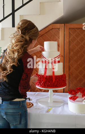 Pasticceria un impilamento 4 tier torta nuziale presso il luogo di ricezione e decorare con commestibili di marzapane rosso fiori Foto Stock