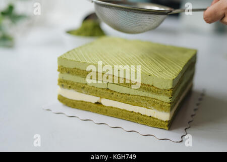 Versare il tè verde in polvere sul delizioso cheesecake Foto Stock