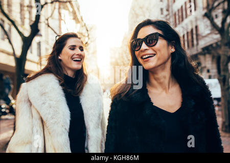 Due donne in vestiti caldi di camminare sulla strada della citta'. Donna sorridente amici all'aperto nella città su un giorno d'inverno. Foto Stock