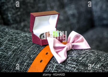 Il govern sofisticati accessori compresi i gemelli nella casella, pelle cintura marrone e rosa il filtro bow tie, posto su un divano grigio Foto Stock