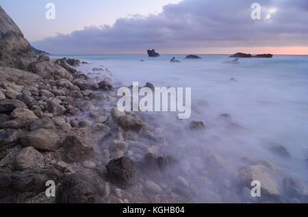 Costa rocciosa immediatamente dopo il tramonto, pietre in onde lattiginoso, acqua ondeggiante. lungo expositure Foto Stock