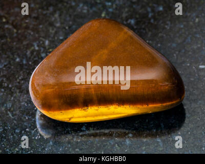 Le riprese in modalità macro di minerale naturale campione di roccia - burattati occhio di tigre pietra preziosa sul granito scuro sfondo dal sud africa Foto Stock