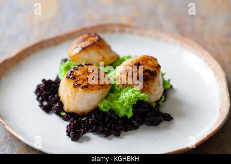 Capesante con nero di riso proibito e purea di piselli Foto Stock