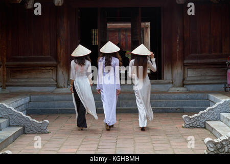 Giovane vietnamita le donne che indossano il tradizionale abito Ao IAM e il cappello conico Non La. camminare dentro il Tempio della Letteratura ad Hanoi, Vietnam Foto Stock