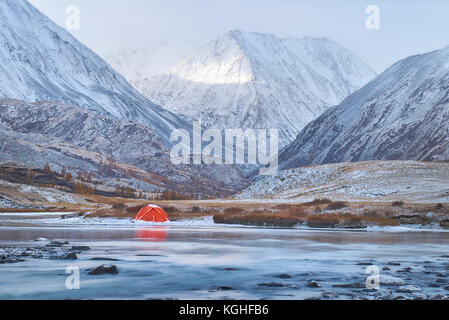 Inverno o tardo autunno in montagna, solitaria di campeggio e di un fiume o di un lago. Tenda Rossa si trova sulla sponda del fiume. Il terreno presenta per essere rocky highland w Foto Stock