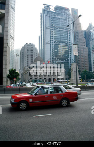 Taxi rosso passa davanti il Cenotafio, ex edificio legislativo e di Hong Kong e Shanghai Bank, Hong Kong, Cina Foto Stock