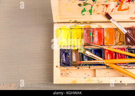 Vernici per disegno, tavolozza e pennello su uno sfondo di legno Foto Stock