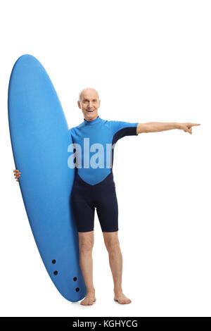 A piena lunghezza Ritratto di un senior in un tipo di muta in possesso di una tavola da surf e puntamento isolati su sfondo bianco Foto Stock