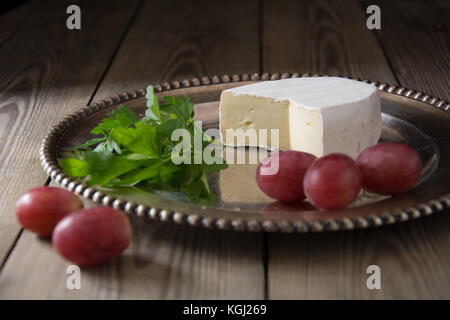 Brie tipo di formaggio su un piatto d'argento con uve ed erbe aromatiche Foto Stock