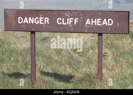 Cartello di avvertimento con la scritta "Danger Cliff Ahead" su terreni erbosi, che avvisa gli escursionisti e i visitatori dei pericolosi bordi delle scogliere nella campagna. Foto Stock