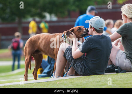 Suwanee GA, Stati Uniti d'America - 6 Maggio 2017: un ragazzo adolescente lascia il suo cane leccare il suo volto con il cane baci a Woofstock, un cane festival a Suwanee centro città. Foto Stock