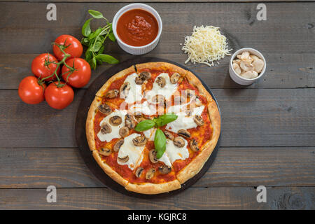 Fresca pizza calda sul tavolo di legno con ingredienti Foto Stock