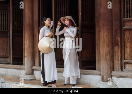 Giovane vietnamita le donne che indossano il tradizionale abito Ao IAM e il cappello conico Non La. ubicazione; Tempio della Letteratura ad Hanoi, Vietnam Foto Stock