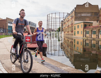 Uomo in bicicletta su una moto di Santander oltrepassa una donna jogging sulla strada alzaia da Regent's Canal a Hackney, a est di Londra, Regno Unito. Foto Stock