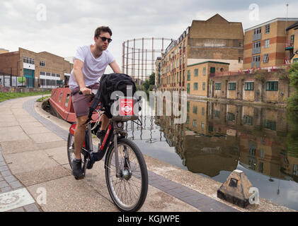 Giovane uomo in estate T-shirt e shorts su Santander noleggio cicli in bicicletta lungo la strada alzaia da Regent's Canal a Hackney, a est di Londra, Regno Unito. Foto Stock