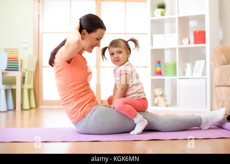 Madre e figlia del bambino sono impegnati nel fitness, yoga e fitness in casa. kid e donna swing premere su stomaco. Foto Stock