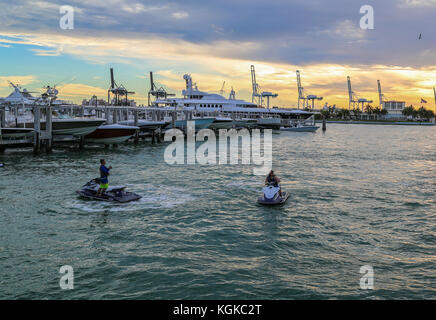 Persone su jet sci in una marina al di fuori di South Beach. Miami, Florida, Stati Uniti d'America con barche e un tramonto tropicale in background. Foto Stock