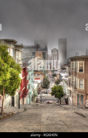 Strada ripida attraverso case, San Francisco, grattacieli nella nebbia, San Francisco, California, Stati Uniti d'America Foto Stock