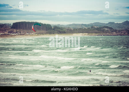 Il kitesurfing uomo in azione sul tramonto burrascosa serata al brusand beach, Norvegia. Foto Stock