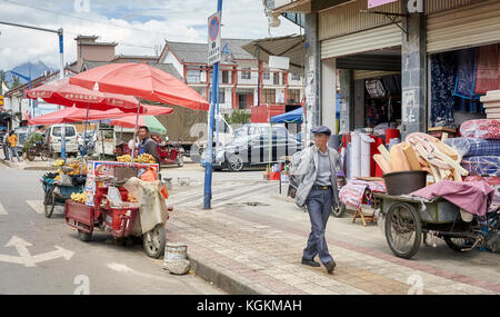 Lijiang, Yunnan, Cina - 28 Settembre 2017: pedonale passa un fornitore di prodotti alimentari con stallo in bicicletta su una strada di Lijiang. Foto Stock
