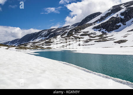 Fusione del ghiaccio del ghiacciaio acqua fluente attraverso la neve e rocce sotto un cielo blu in Norvegia Foto Stock
