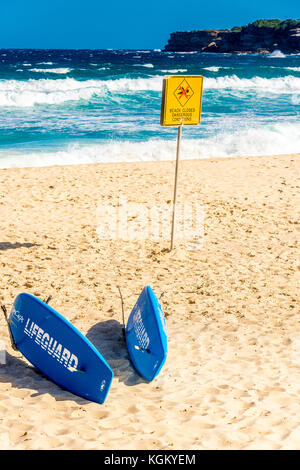 Lifeguard Rescue Boards riposano sulla sabbia con pericolose condizioni di surf in background a Tamarama Beach a Sydney, NSW, Australia Foto Stock