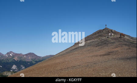 Lone rider permanente sulla cima della montagna godendo la vista, i suoi cavalli nelle vicinanze. Sud Chilcotin Mountain Park, British Columbia, Canada Foto Stock