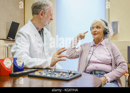Senior paziente che indossa le cuffie parlando di Audiologist durante l orecchio esame presso l'ufficio del medico Foto Stock