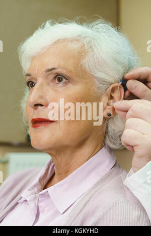 Audiologist assistere senior donna in inserimento di protesi in cliniche Foto Stock