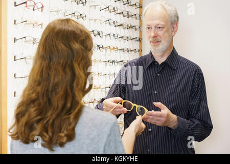 Proprietario maturo che mostra occhiali da donna con capelli castani in negozio Foto Stock