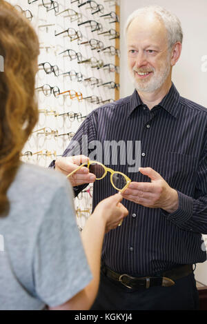 Proprietario sorridente dando occhiali per donna in negozio Foto Stock