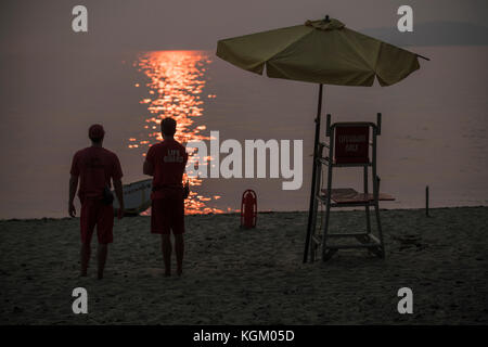 Vista posteriore dei bagnini in piedi in spiaggia durante il tramonto Foto Stock