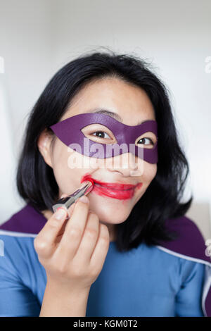 Ritratto di donna sorridente supereroe indossando un rossetto rosso contro lo sfondo grigio Foto Stock
