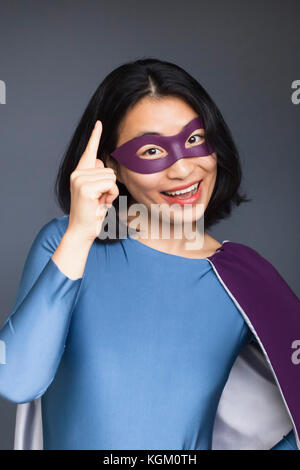 Ritratto di Allegro supereroe femminile gesticolando mentre in piedi contro lo sfondo grigio Foto Stock