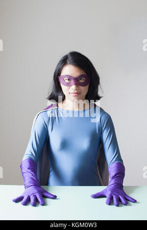 Ritratto di fiducioso giovane donna vestita come supereroe contro il muro bianco Foto Stock