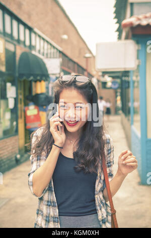 Asian più giovane donna shopping e parlando di smart phone con volto sorridente felicità emozione Foto Stock