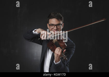 Fiducioso sorridente giovane uomo suona il violino mentre in piedi su sfondo nero Foto Stock