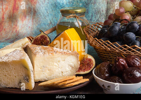 Composizione alimentare con blocchi di formaggio ammuffito, prugne in salamoia grappolo di uva, cracker, figure blu su sfondo rosso. Foto Stock