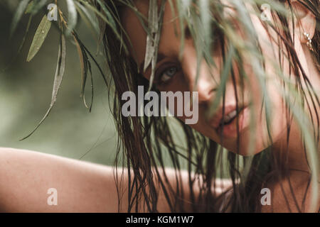Close-up ritratto di giovane donna con capelli bagnati cercando attraverso foglie Foto Stock