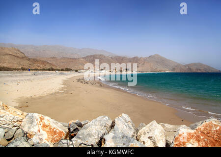 Vista su una spiaggia sporca in oman, soleggiata giornata calda, al hajar montagne sullo sfondo, nessun popolo Foto Stock