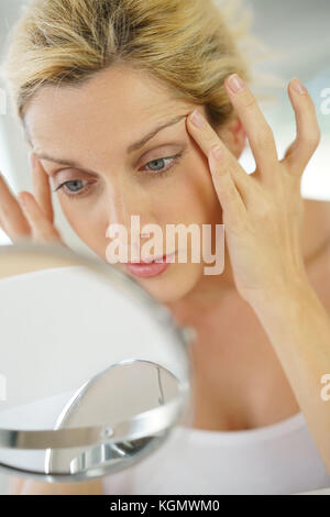 Di mezza età donna bionda applicando anti-invecchiamento della crema nella parte anteriore dello specchio Foto Stock